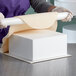 A person rolling out a piece of foam using a Baker's Mark foam square cake dummy.