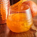 A glass of orange liquid with Spirdust Copper Cocktail Shimmer on a table.