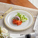 A Visions ivory plastic plate with gold bands, a fork, and a knife on a table.