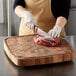 A person cutting meat on a Fox Run acacia wood chopping block.