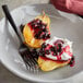 A plate with a spoon and IQF black currants, whipped cream, and fruit topping.