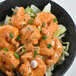 A bowl of shrimp with sauce and green onions with a white background.