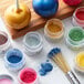 A jar of apple green powder on a table with other colorful powders and a brush.