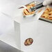 A gloved hand using a knife to cut a pastry into a white circular candy box.