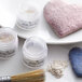 A white heart-shaped container of Roxy & Rich Violet Pearl Lustre Dust with a brush on top.