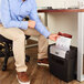 A man sitting in a chair and using a black and silver GBC ShredMaster paper shredder to shred paper.