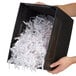 A person holding a black box with shredded paper.