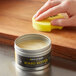 A hand using a yellow sponge to clean Epicurean board butter.