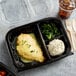 A black 11" x 8 1/2" plastic hinged container with 3 compartments filled with food.