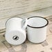 Two white Crow Canyon Home enamelware mugs with black rims on a table.