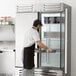 A man in a white shirt and black apron opening a Beverage-Air reach-in freezer with a slate finish.