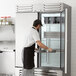 A man wearing a white shirt and black apron opening a Beverage-Air reach-in refrigerator.