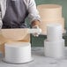 A woman using a rolling pin to make a cake over round white cake dummies.