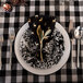 A white enamelware plate with a black rim, silverware, and a napkin on it.