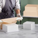 A person rolling a piece of white foam on a white block.