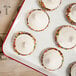 A white rectangular enamelware tray with red rolled rim holding white frosted desserts with sprinkles.
