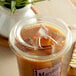 A plastic cup of iced tea with a Fabri-Kal Greenware clear plastic strawless lid next to a plant.