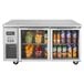 A Turbo Air undercounter refrigerator with glass doors filled with fruit and juice containers.