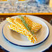 A Crow Canyon Home white enamelware plate with a blue rolled rim and a napkin on it.