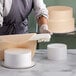 A woman using a rolling pin on a stack of white round cake dummies.