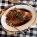 A white enamelware oval platter with meat, a fork, and a knife.