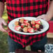 A person holding a Crow Canyon Home white enamelware oval plate with fruit.