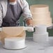 A woman using a rolling pin to roll out a cake on a white table.