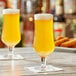 Two Acopa Select stemmed beer glasses filled with beer on a table in a bar.