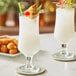 Two Acopa Select stemmed beer glasses with white liquid and pineapple garnish.