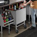 A man standing behind a Regency stainless steel portable ice bin on a counter in a cocktail bar.