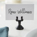 An American Metalcraft black metal low profile harp table card holder with a place card that reads "Ryan Williams" on a white table.