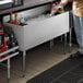 A man standing next to a Regency underbar ice bin with bottle holders on a counter.