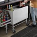 A man standing next to a Regency stainless steel portable ice bin on a counter.