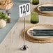 A table with a stainless steel harp card holder with a number on it and a plate.