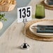 An American Metalcraft stainless steel harp table card holder with a number plate on a table.
