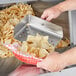 A person holding a metal pan with tortilla chips in a ServIt chip warmer.