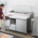 A woman using an Avantco refrigerated pizza prep table with drawers to store pizza.