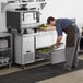 A man in a professional kitchen putting food in the left drawer of a stainless steel Avantco undercounter refrigerator.