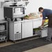 A man in a professional kitchen using an Avantco stainless steel undercounter refrigerator drawer.