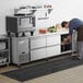 A man putting food into an Avantco undercounter refrigerator with drawers.