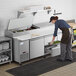 A woman in an apron using an Avantco pizza prep table to put food in a tray.