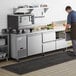 A man in a professional kitchen opening an Avantco stainless steel worktop refrigerator with drawers.