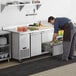 A man putting food into a drawer in a stainless steel Avantco worktop refrigerator.