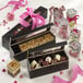 A Solia wooden case filled with chocolate macarons on a white table with a pink ribbon.