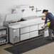 A woman using an Avantco 6 drawer refrigerated pizza prep table in a commercial kitchen.