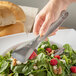 A person using Carlisle stainless steel bread tongs to serve bread at a table with salad.