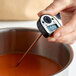 A hand using a Comark DT300 digital pocket probe thermometer to check the temperature of liquid in a pot.