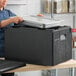 A woman in a professional kitchen using a Cambro black top-loading food pan carrier.