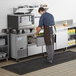 A man in a blue shirt and apron working in a commercial kitchen with an Avantco stainless steel worktop refrigerator.