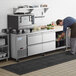 A man using an Avantco stainless steel worktop refrigerator in a professional kitchen.